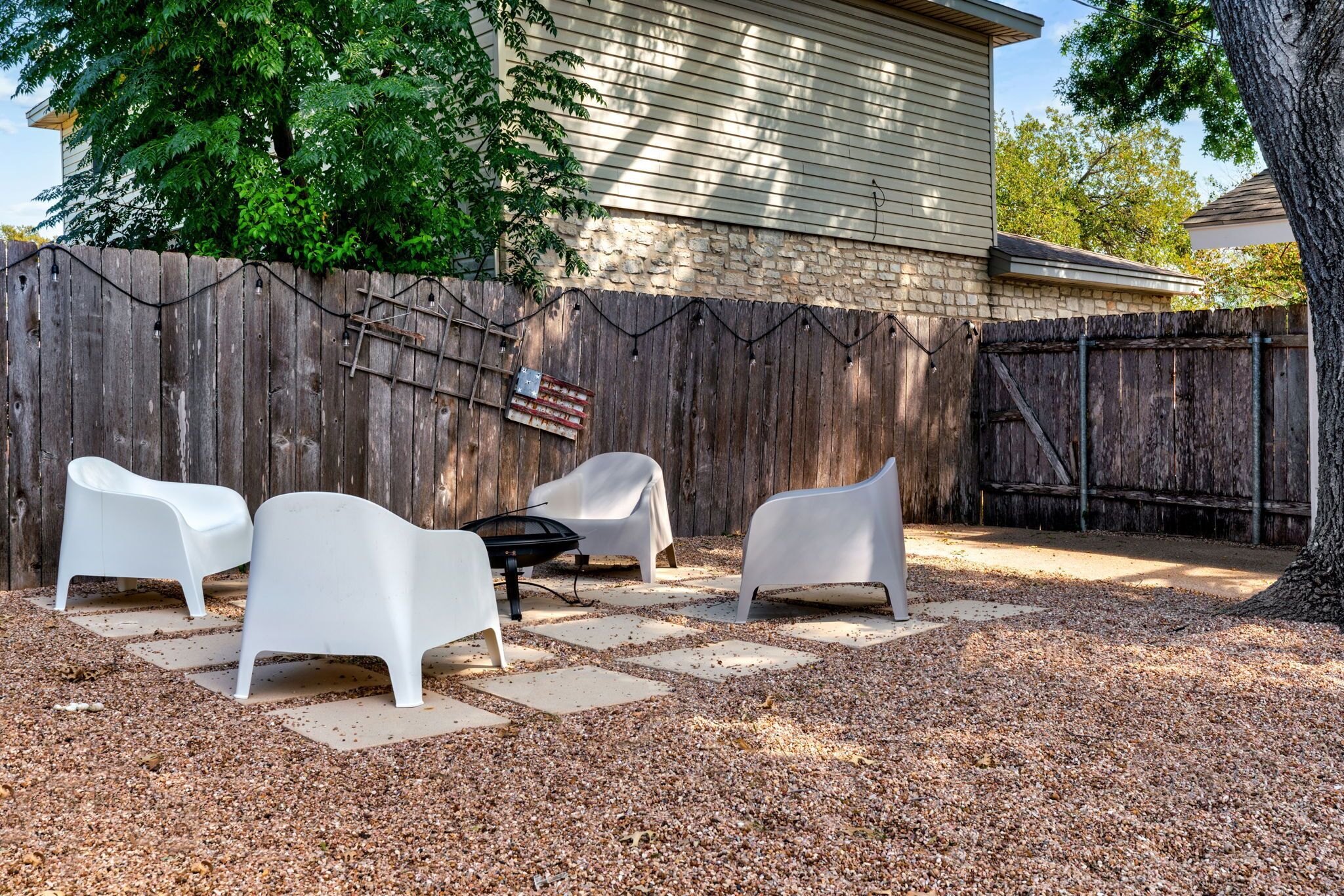 Un jardin avec une clôture en bois, un foyer et des chaises en plastique blanc.
