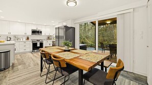 A modern kitchen with white cabinetry, a stainless steel refrigerator, and a dining area with a wooden table and chairs.