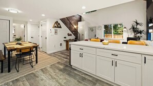 A modern kitchen with white cabinetry, a wooden dining table, and a staircase leading to a loft area.