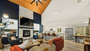 A modern living room with a fireplace, a dining area, and a kitchen with white cabinets and stainless steel appliances.