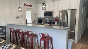 Una cocina moderna con armarios blancos, electrodomésticos de acero inoxidable y taburetes de bar rojos.