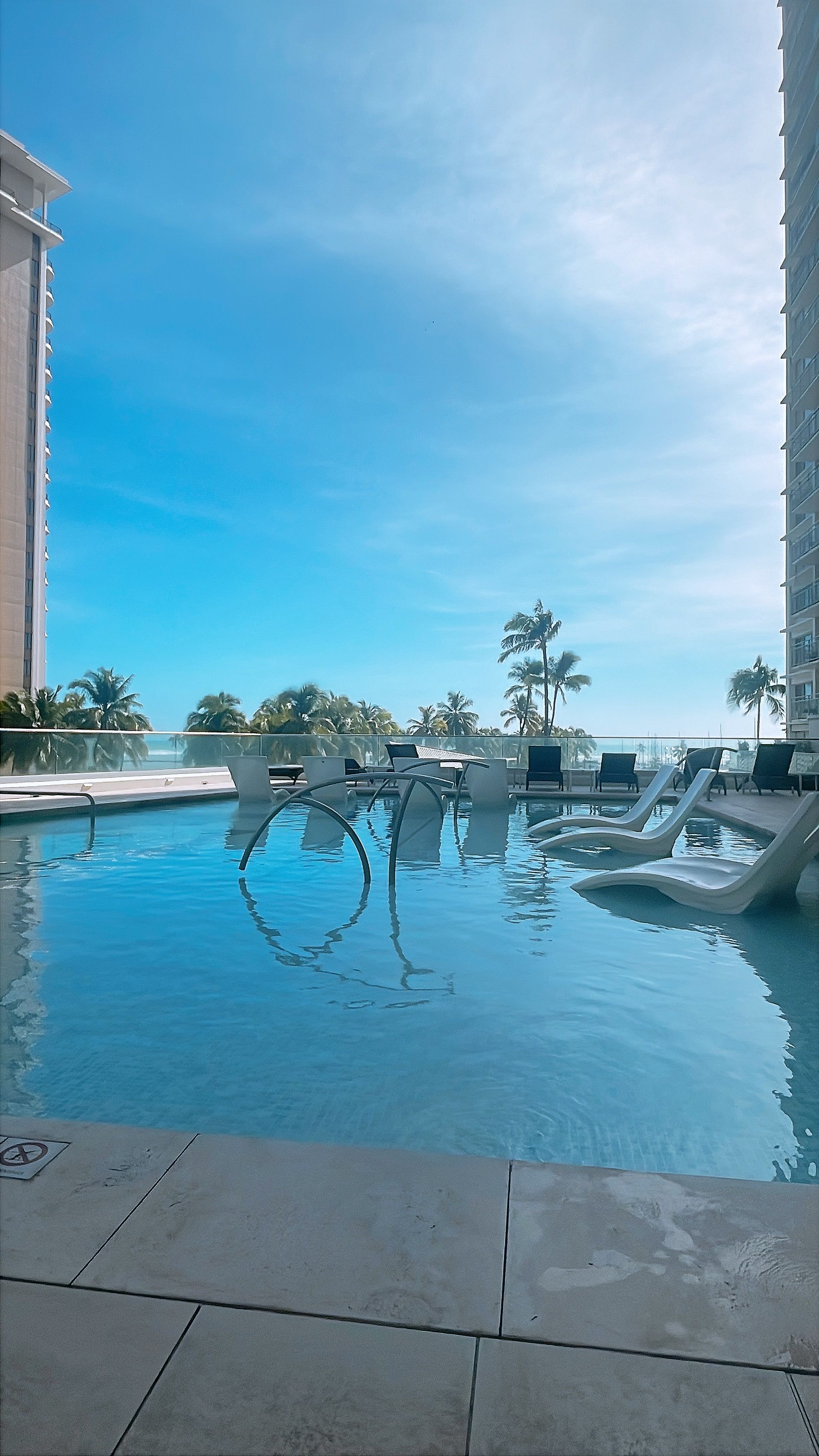 A swimming pool with lounge chairs and palm trees in the background.