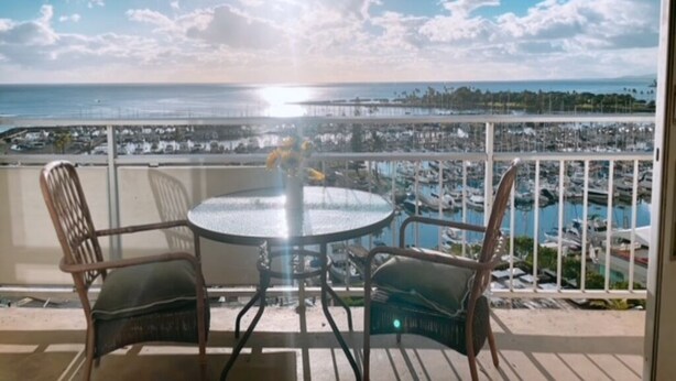 A balcony with a round table and two chairs, overlooking a marina with boats and a distant shoreline. - Waikiki ocean view studio, easy walk to beach, shopping, restaurants (Honolulu)