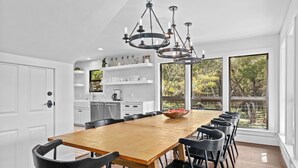 A modern kitchen with a wooden dining table, black chairs, and a chandelier. - Summer Riverfront | 5 Acres | Hot Tub | Sleeps 17 (Wimberley)