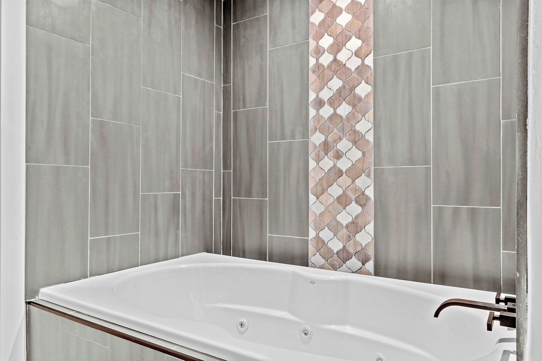 A modern bathroom with a freestanding bathtub, grey tiles on the walls, and a decorative tile pattern on the back wall.
