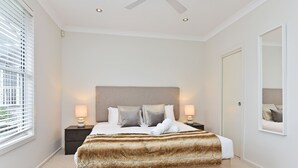 Un dormitorio con una cama grande, dos lámparas de noche, un cabecero y un espejo en la pared.