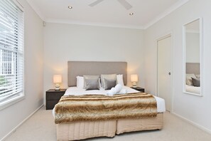 Un dormitorio con una cama grande, dos lámparas de noche, un cabecero y un espejo en la pared.