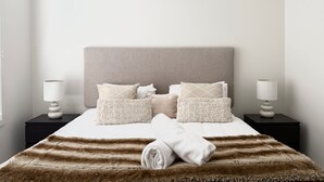 Una cama bien hecha con un edredón a rayas, cabecera y varias almohadas.