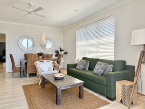 A modern living room with a green sofa, wicker chairs, a wooden coffee table, and a ceiling fan.