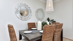 Un comedor con mesa de madera oscura, sillas de mimbre y dos espejos de pared decorados.