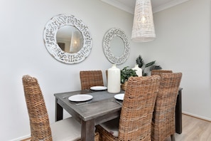 Un comedor con mesa de madera oscura, sillas de mimbre y dos espejos de pared decorados.