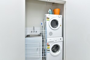 A front-loading washer and dryer unit with a water rating label, a metal drying rack, and a small orange bucket.
