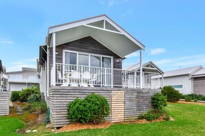 A modern two-story house with a covered balcony, a small garden, and a clear sky. - Azure Tides at Caves Beach Villas (Caves Beach)