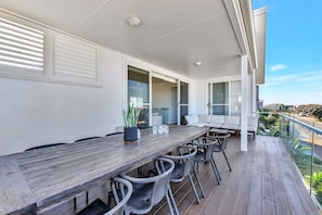 A covered outdoor dining area with a wooden table and chairs, a potted plant, and a view of the street.