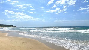 A beach with waves, a clear sky, and a distant landform. - Bombora Beach House at Caves Beach (Caves Beach)