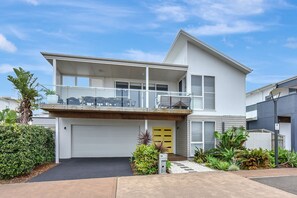 A two-story residential building with a balcony, a garage, and a well-maintained garden.