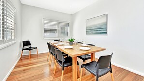 A dining area with a wooden table set for four, surrounded by black chairs with wooden legs. - Bombora Beach House at Caves Beach (Caves Beach)