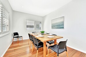 A dining area with a wooden table set for four, surrounded by black chairs with wooden legs. - Bombora Beach House at Caves Beach (Caves Beach)