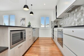 A modern kitchen with wooden cabinetry, stainless steel appliances, and a herringbone tile backsplash. - Bombora Beach House at Caves Beach (Caves Beach)