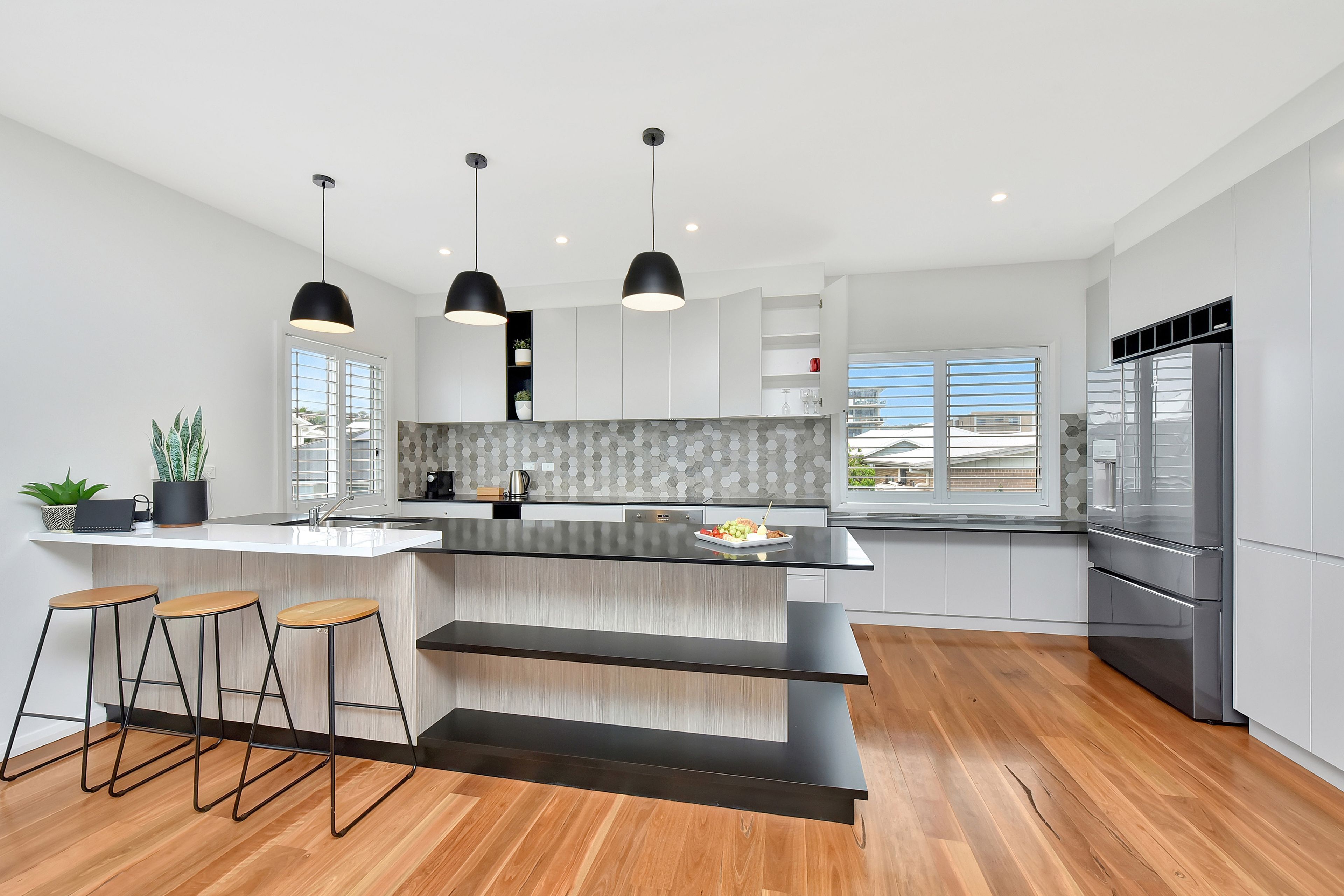 A modern kitchen with a large island, bar stools, pendant lights, and a stainless steel refrigerator.