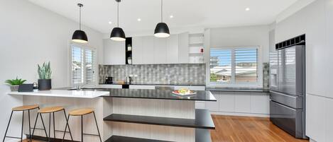A modern kitchen with a large island, bar stools, pendant lights, and a stainless steel refrigerator.