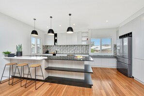 A modern kitchen with a large island, bar stools, pendant lights, and a stainless steel refrigerator.