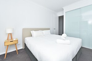 A modern hotel room with a large bed, a bedside table with a lamp, and a glass door leading to a bathroom. - Bombora Beach House at Caves Beach (Caves Beach)