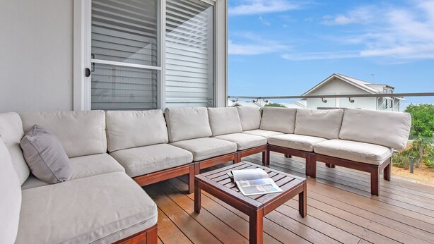 A covered outdoor seating area with a sectional sofa and a wooden table, overlooking a residential area. - Bombora Beach House at Caves Beach (Caves Beach)