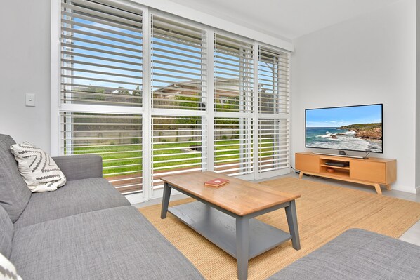 A modern living room with a grey sofa, a wooden coffee table, and a television on a wooden stand.