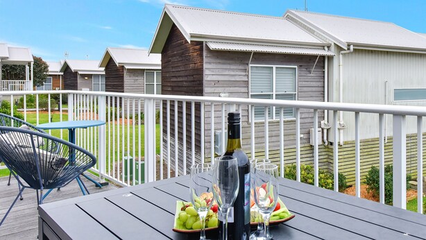 A deck with a table set for a meal, a bottle of wine, and two glasses. - Mariner's Rest at Caves Beach Villas (Caves Beach)