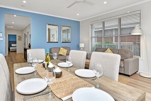 Un coin repas avec une table dressée pour quatre personnes, deux canapés, un ventilateur de plafond et une fenêtre avec des stores.