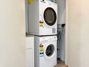 A compact laundry area with two stacked washing machines, a drying rack, and a white wall.