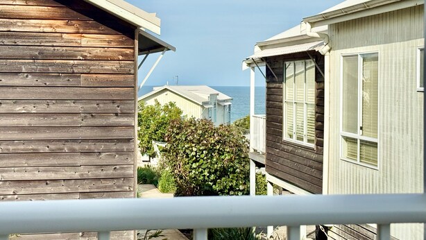 Een houten gebouw met een balkon, naast een wit gebouw met een raam, met uitzicht op een waterpartij.