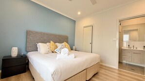 Een slaapkamer met een bed, nachtkastje en een badkamer zichtbaar door een geopende deur.