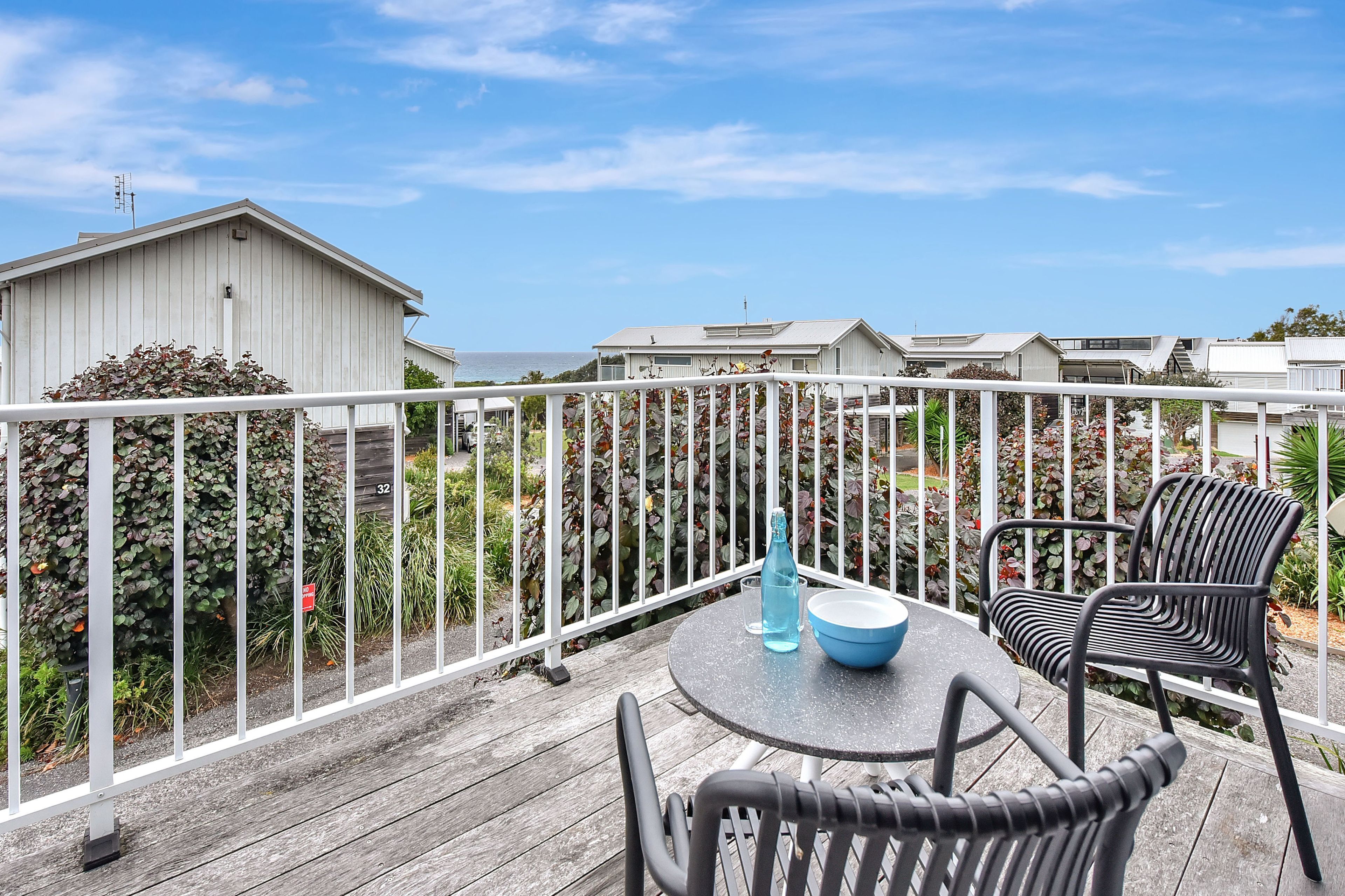 A deck with outdoor furniture, a table, and a chair, overlooking a residential area with houses and a clear sky.