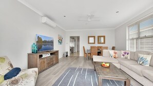 Una sala moderna con un sofá, una mesa de centro y un televisor.  Hay una zona de comedor con una mesa y sillas.
