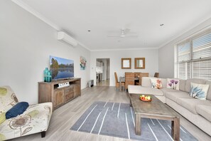 Un salon moderne avec un canapé, une table basse et un téléviseur. Il y a également un coin repas avec une table et des chaises.
