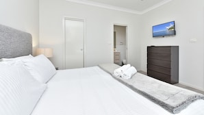 Habitación de hotel con cama, televisor montado en la pared, armario y baño visible a través de una puerta abierta.