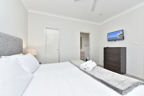 Une chambre d’hôtel avec un lit, un téléviseur fixé au mur, une armoire et une salle de bain visible à travers une porte ouverte.