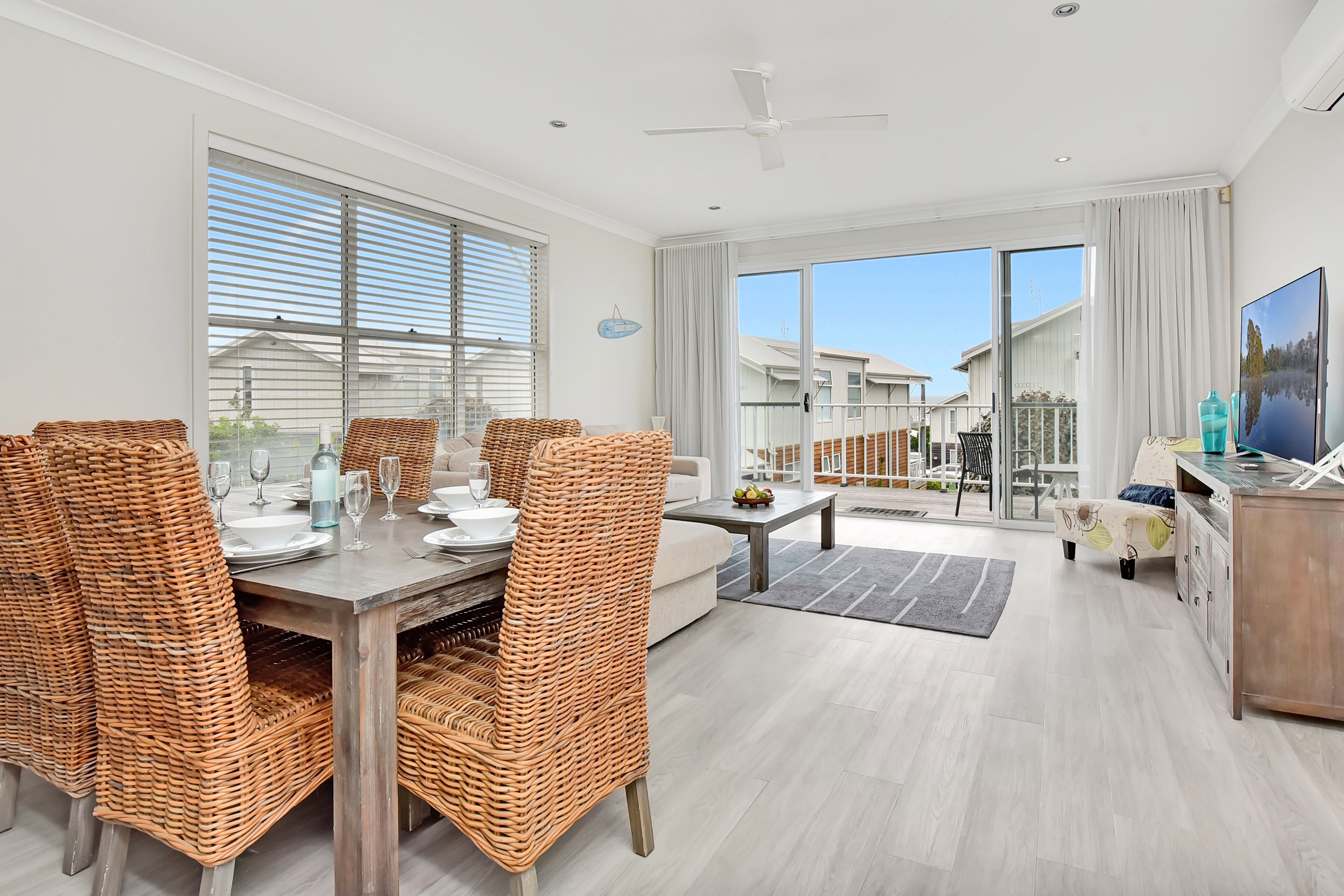 A modern living room with a dining area, large windows, and a view of the outside.
