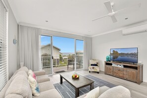 Un salon spacieux comprenant un canapé, une table basse, un téléviseur et un balcon avec vue sur la mer.