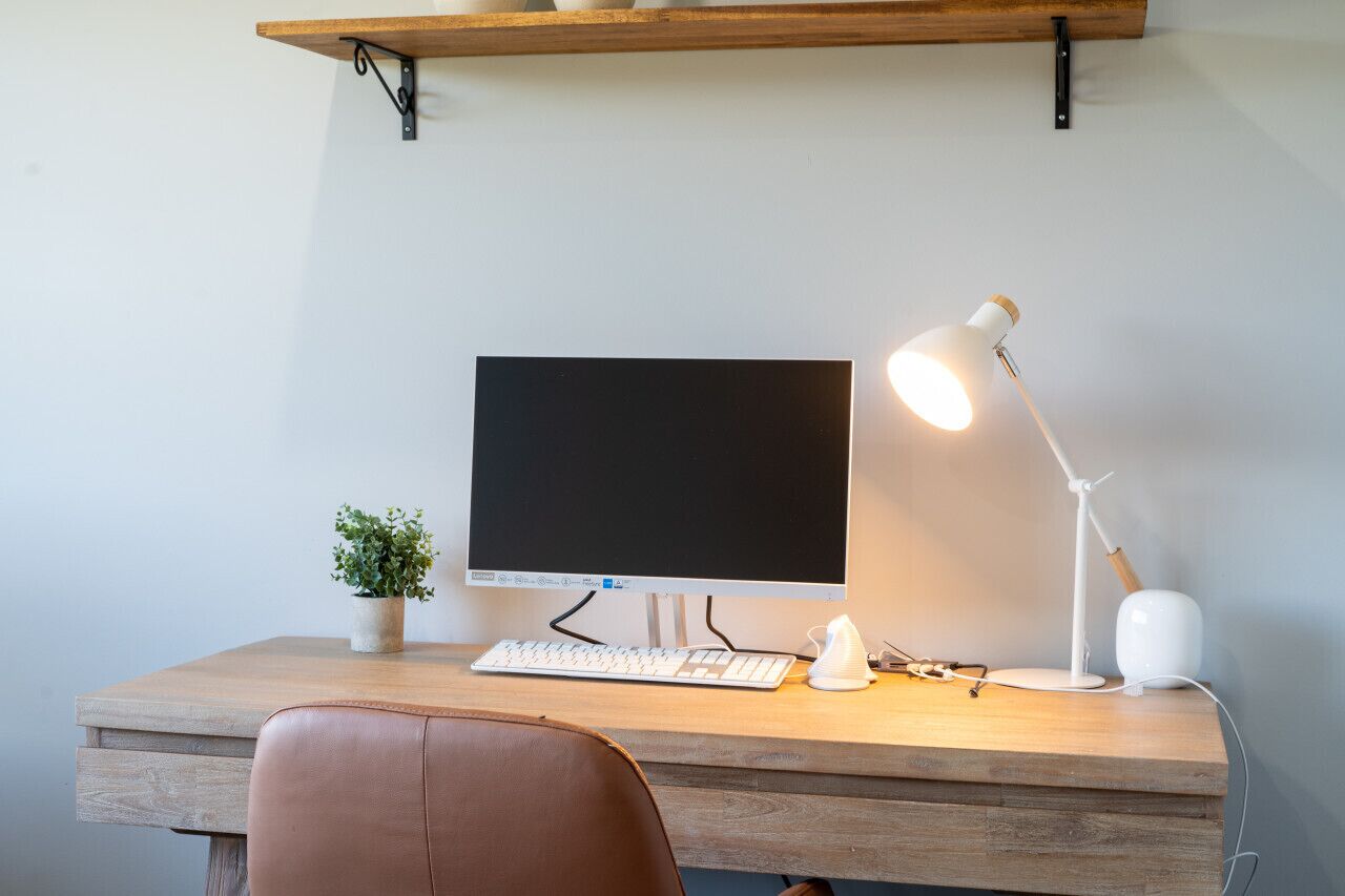 A wooden desk with a desktop computer, keyboard, and a white desk lamp.