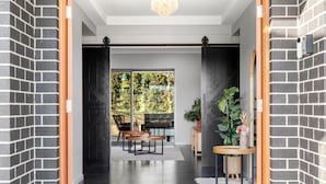 Un interno moderno con una parete in mattoni scuri, una porta in legno e vista su un patio esterno con tavolo e sedie.