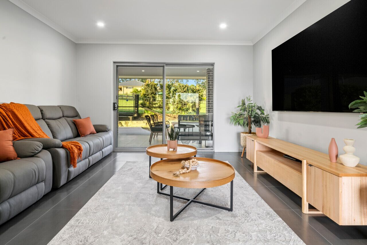 A modern living room with a grey sofa, two wooden coffee tables, a wooden console table, and a large TV on the wall.