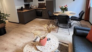 A modern kitchen with dark cabinets, a microwave, and a coffee machine. There is a dining area with a round table and chairs, and a living room with a sofa and a coffee table. - "Atelier du spa" in the heart of Avranches near Mont Saint Michel  (Avranches)