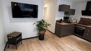 A modern kitchen with a flat-screen TV, a small side table, a potted plant, and a built-in oven. - "Atelier du spa" in the heart of Avranches near Mont Saint Michel  (Avranches)
