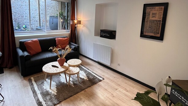 A modern living room with a black sofa, a small round table, and a large window. - "Atelier du spa" in the heart of Avranches near Mont Saint Michel  (Avranches)