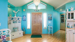 A room with teal walls, wooden flooring, a wooden door, a chandelier, a small table, a cabinet, and various decorative items.