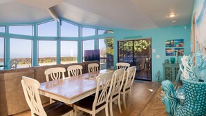A dining area with a wooden table and white chairs, large windows with a view, and a blue decorative piece on the right.
