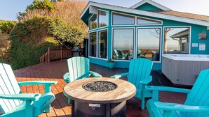 A cozy outdoor deck with a fire pit, turquoise Adirondack chairs, and a hot tub.